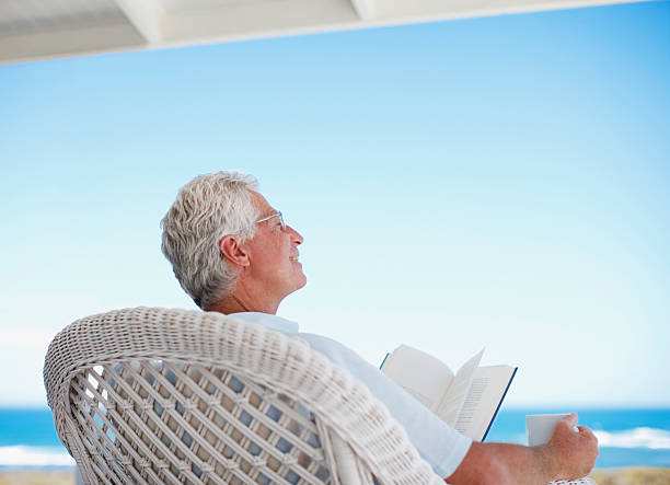 uomo anziano legge un libro sulla spiaggia, con patio - men reading outdoors book foto e immagini stock