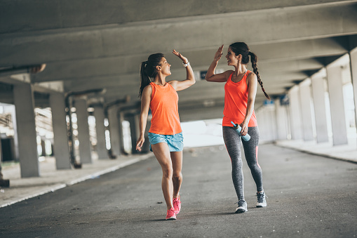 Two young woman giving high five to each other.They relaxing after jogging on street.