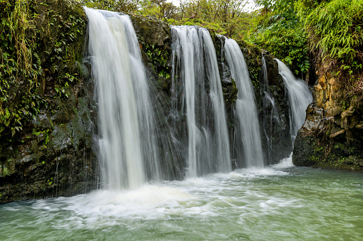 Strong and broad waterfalls flowing into a clear green pond in Puaa Kaa State Wayside Park at side of the Road to Hana Highway, Maui, Hawaii, USA.