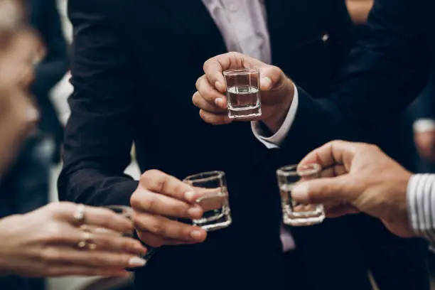 Photo of people toasting holding glasses of vodka cheering at wedding reception, celebration outdoors, catering in restaurant. christmas and new year