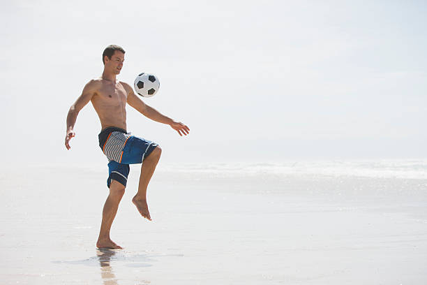 hombre saltando pelota de fútbol en la playa - beach football fotografías e imágenes de stock