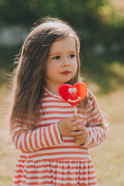 赤いハート型のキャンディを持つかわいい女の赤ちゃん。 - child valentines day candy eating ストックフォトと画像