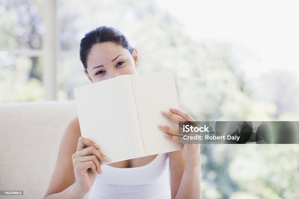 Woman holding book over mouth  Hiding Stock Photo
