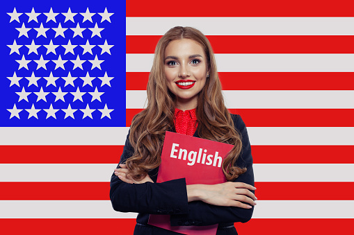 Pretty woman student smiling and holding book against the United States of America flag background. Travel USA and learn american english language