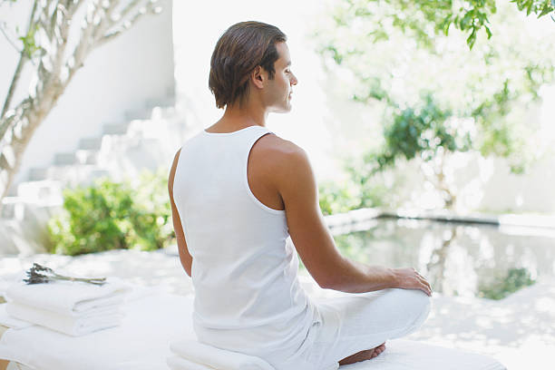 homem sentado com as pernas cruzadas à beira da piscina - men yoga meditating cross legged - fotografias e filmes do acervo