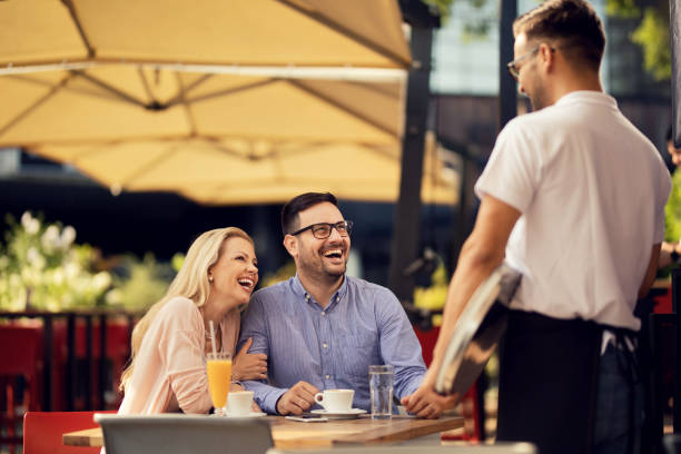 istock Happy couple laughing while talking to a waiter in a cafe, 1163789843