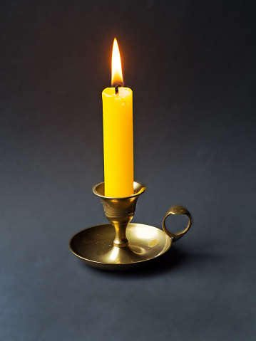 lit candle in a candlestick on a black background,