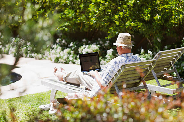 senior man on lounge chair using laptop - 銀髮族網民 個照片及圖片檔