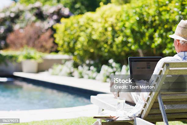 Senior Hombre Usando Una Computadora Portátil En El Diván En Junto A La Piscina Foto de stock y más banco de imágenes de Hombres mayores