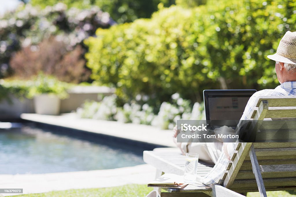 Senior homme avec ordinateur portable sur une chaise longue au bord de la piscine - Photo de Hommes seniors libre de droits