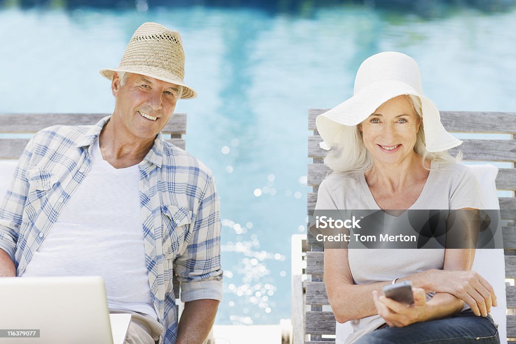 Senior par usando ordenador portátil y teléfono móvil en la piscina - Foto de stock de Mujeres libre de derechos