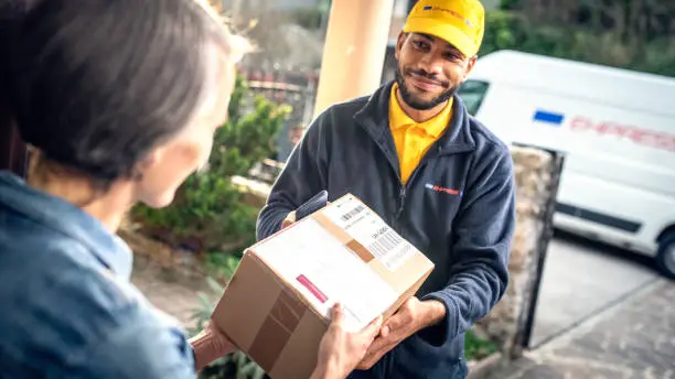 Smiling beard African American delivery man giving cardboard box to a woman at doorway.