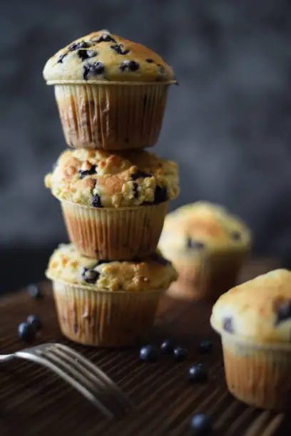 Crumble top blueberry muffins in pile on oak board on dark background with natural lighting copy space