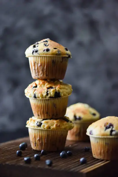 Stable pile of crumble top blueberry muffins on oak board on dark background with natural lighting copy space