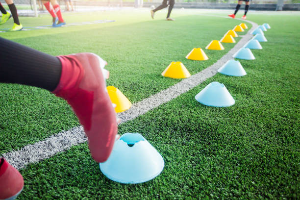 istock Multi color marker cones on green artificial turf with blurry soccer player  moving speed test and Jogging and jump between it. 1163809894