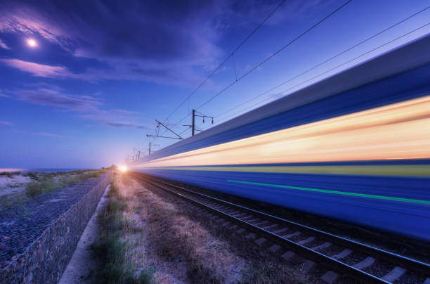 istock High speed passenger train in motion on the railroad at summer night. Moving blurred modern commuter train at dusk. Railway station and purple sky with moon and clouds. Industrial landscape. Transport 1163810133