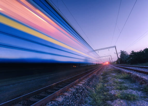 istock High speed passenger train in motion on the railroad at summer night. Moving blurred modern commuter train at dusk. Industrial landscape with railway station and purple sky. Transport.  Travel 1163810240