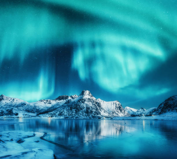 aurora boreal sobre montañas nevadas, costa marina congelada y reflejo en el agua en las islas lofoten, noruega. las auroras boreales. paisaje invernal con luces polares, hielo en el agua. cielo con estrellas y aurora - islandia fotografías e imágenes de stock