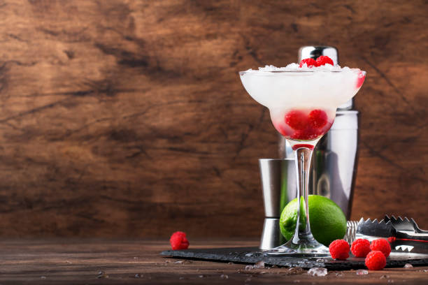 himbeer-daiquiri, alkoholischer cocktail mit weißem rum, limettensaft, himbeeren und zerkleinertem eis aus hohem glas, auf holzstangentheke mit stahlstangenwerkzeugen - crushed ice freshness red lime stock-fotos und bilder