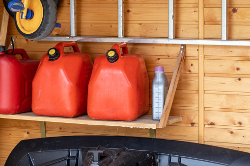 Esquina de garaje con tres latas de combustible de plástico rojo, escalera y arado de nieve para atv con pared de madera en el fondo. Contenedores de gasolina reservaalmacenamiento en el garaje de la casa del vehículo photo