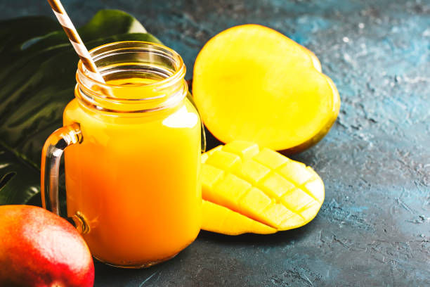 istock Mango juice or cocktail in glass jar with fresh fruit on blue tropical background, copy space, selective focus 1163813941