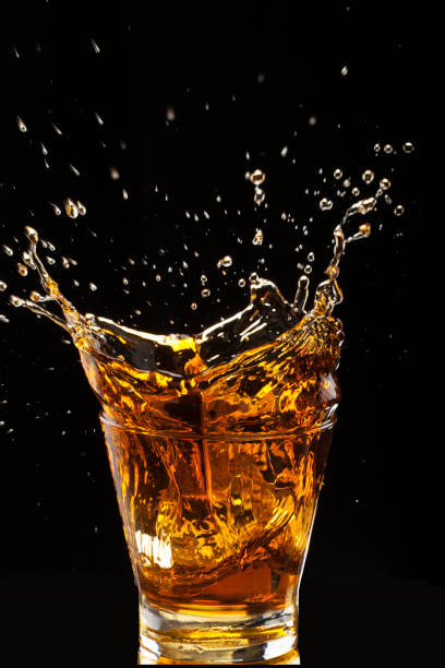 Hard drink splashing Close-up of a glass with gold colored alcoholic drink, such as whiskey, rum, brandy or cognac. glass of bourbon stock pictures, royalty-free photos & images
