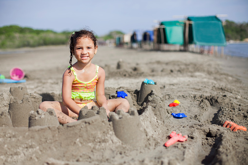 Girl of latin ethnicity sitting on the sand building sandcastles with buckets and shovels.