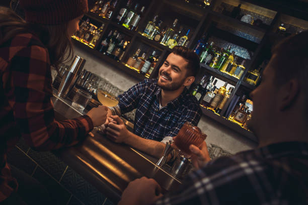 istock Young bartender standing at bar counter with visitors drinking cocktails having nice conversation 1163828256