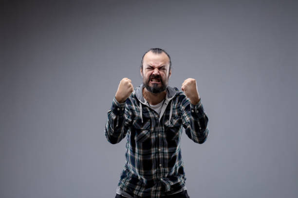 Man in a rage gnashing his teeth Man in a rage gnashing his teeth and balling his fists as he bends towards the camera with a vindictive expression, isolated on grey with copy space italian music stock pictures, royalty-free photos & images