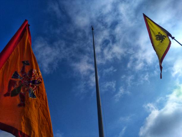 istock Two flags with flagpole and one flagpole without flag isolated on blue and cloudy sky. 1163841519