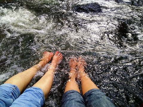 Two pairs of ladies legs immersed in cold running water of a river on a sunny day