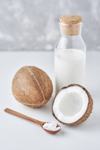 istock Coconut milk in glass bottle and fresh coconuts with half on a gray background 1163857600