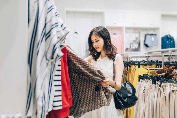 giovane donna asiatica che sceglie nuovi vestiti nel negozio di abbigliamento. - shopping clothing store women retail foto e immagini stock