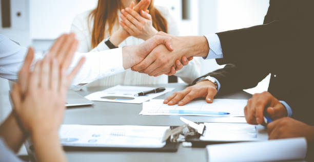 istock Business people shaking hands at meeting while theirs colleagues clapping and applauding. Group of unknown businessmen and women in modern white office. Success teamwork, partnership and handshake concept 1163862832