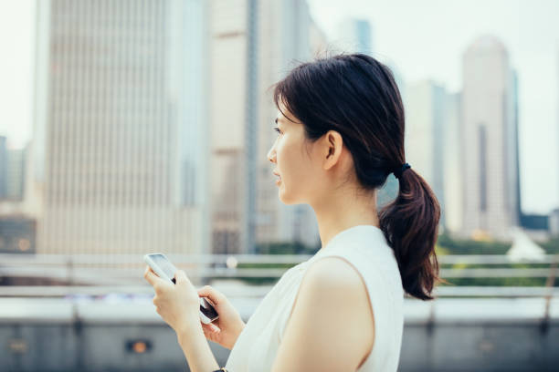 joven empresaria asiática que usa un teléfono inteligente al aire libre frente a los rascacielos financieros en el distrito financiero de lujiazui, shanghai, china - china shanghai business people fotografías e imágenes de stock