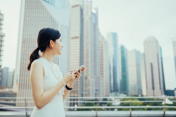 joven empresaria asiática que usa un teléfono inteligente al aire libre frente a los rascacielos financieros en el distrito financiero de lujiazui, shanghai, china - china shanghai business people fotografías e imágenes de stock