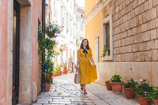 tourist woman in yellow sundress walking by small croatian city street. summer vacation concept