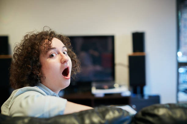 young woman watching tv looks round to camera, horrified - gasping imagens e fotografias de stock