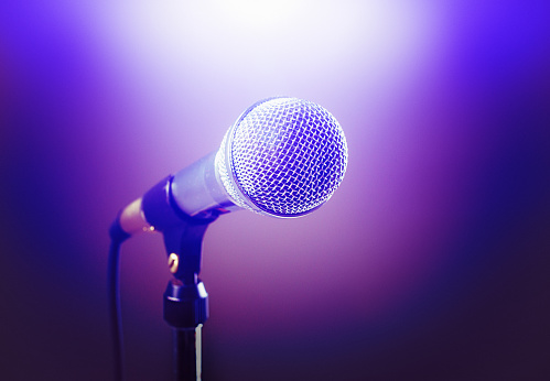 A dramatically lit stage microphone, purple spot lit in white.