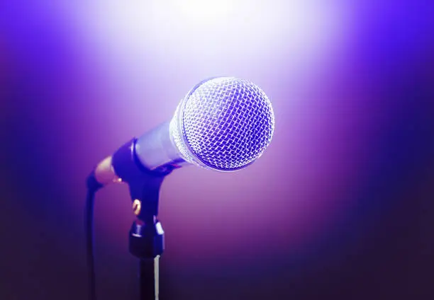 Photo of Stage microphone dramatically lit in purple and spot lit in white