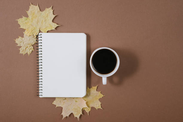 istock Workspace with golden maple leaves, bumps, notebook and cup of coffe on brown background. Creative composition. Autumn or Winter concept. Flat lay, top view 1163884342