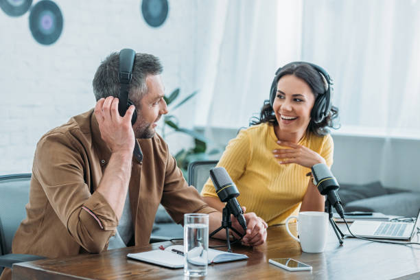 two cheerful radio hosts in headphones recording podcast in broadcasting studio two cheerful radio hosts in headphones recording podcast in broadcasting studio podcast stock pictures, royalty-free photos & images