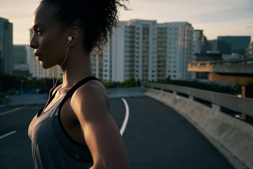 Cropped shot of an attractive young woman wearing earphones and standing outside in the city after her morning run