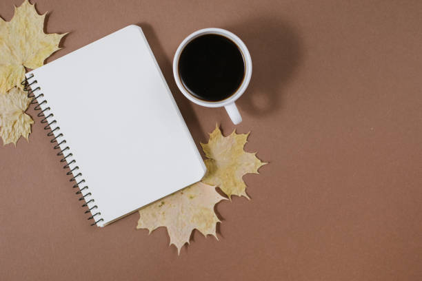 istock Workspace with golden maple leaves, bumps, notebook and cup of coffe on brown background. Creative composition. Autumn or Winter concept. Flat lay, top view 1163886931
