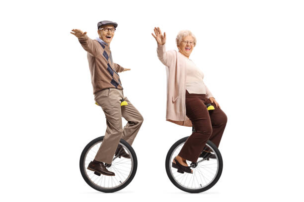 elderly man and woman riding unicycles and smiling at the camera - unicycle unicycling cycling wheel imagens e fotografias de stock