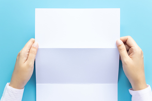 hand holding blank white paper for letter mock up, isolated on blue background with copy space. studio shot