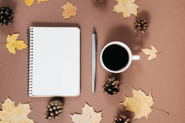 istock Workspace with golden maple leaves, coffee cup, bumps, notebook and pen on brown background. Creative composition. Autumn or Winter concept. Flat lay, top view 1163890161