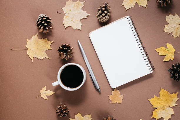 istock Autumn composition. Golden maple leaves, coffee cup, bumps, notebook and pen on brown background. Autumn or Winter concept. Flat lay, top view 1163891273