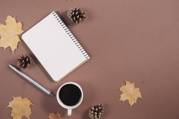 istock Autumn composition. Golden maple leaves, coffee cup, bumps, notebook and pen on brown background. Autumn or Winter concept. Flat lay, top view 1163891291