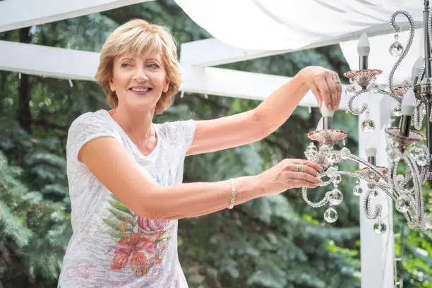 happy senior Woman changing a light bulb in a chandelier outdoor